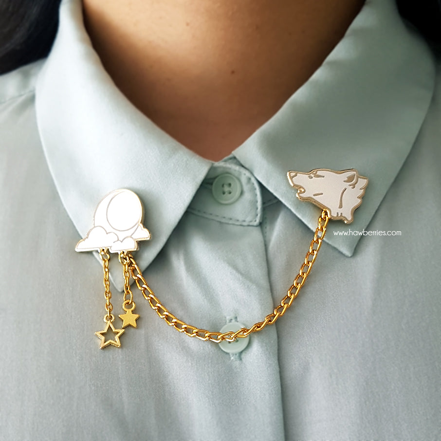 The white variation of Wolf & Moon collar pins on model with pastel mint button up. White wolf howling enamel pin is connected to white moon and clouds by golden delicate chain with tiny star charm.