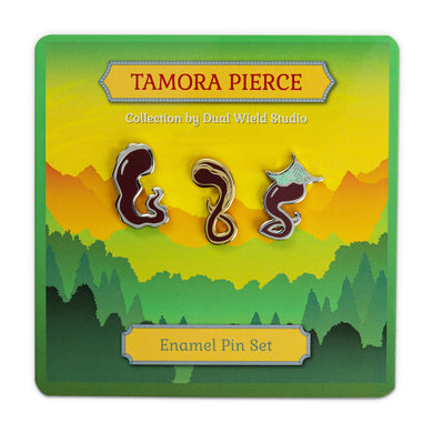 All three Darking enamel pins (Jelly, Gold-Streak, and Leaf) on green Tamora Pierce backing card. Jelly is squiggly, Gold-Streak is a gold enamel pin with ribbons of gold running through it, and Leaf wears a light green leaf on its head. White background.
