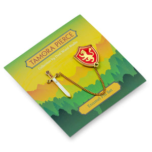 Angled view of the Tamora Pierce Alanna Sword & Shield pins on yellow and green forest illustrated backing card.