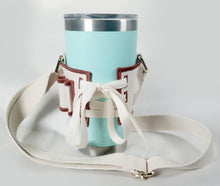 Load image into Gallery viewer, Back view of lacing on Linen color cloth cup holder with Baker Bunneh as an embroidered patch holding a mint green coffee tumbler.