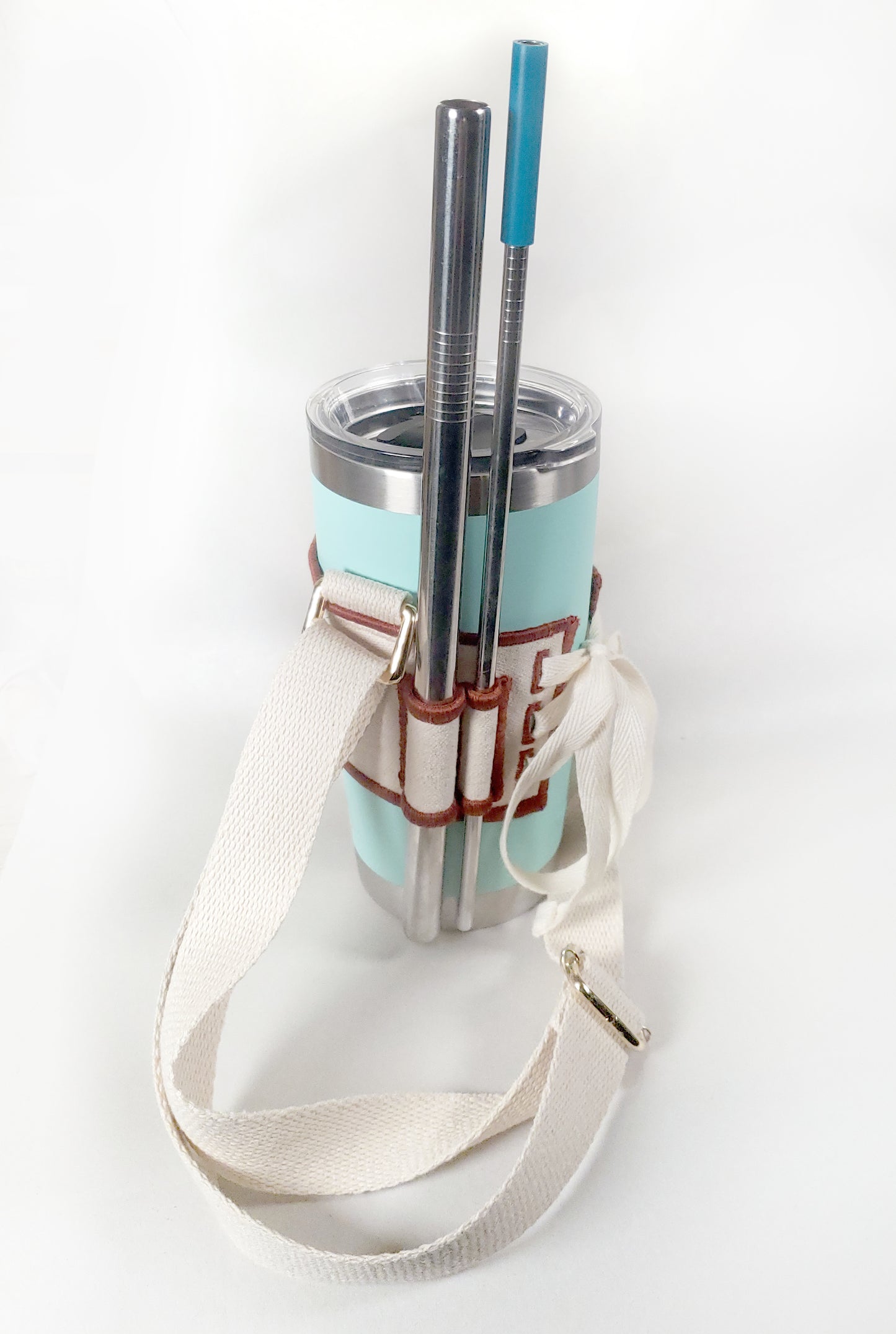 Linen color cloth cup holder with Baker Bunneh as an embroidered patch holding a mint green coffee tumbler and metal straw.