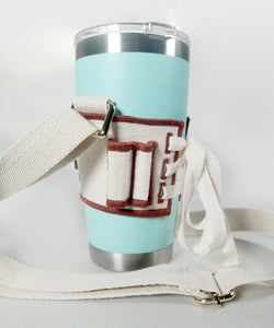 Side view of Linen color cloth cup holder with Baker Bunneh as an embroidered patch holding a mint green coffee tumbler.