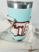 Load image into Gallery viewer, Closeup of Linen color cloth cup holder with Baker Bunneh as an embroidered patch holding a mint green coffee tumbler.