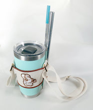 Load image into Gallery viewer, Linen color cloth cup holder with Baker Bunneh as an embroidered patch holding a mint green coffee tumbler and metal straw..