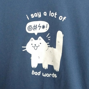 Slate blue shirt with a white printed design of a cat and speech bubble containing a grawlix. Printed around the cat is, "i say a lot of bad words."