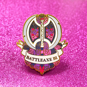 The goldcast pin features a dual bladed axe and roses in the colors of the bisexual flag. A ribbon trails across the front and reads "Battleaxe Bi."