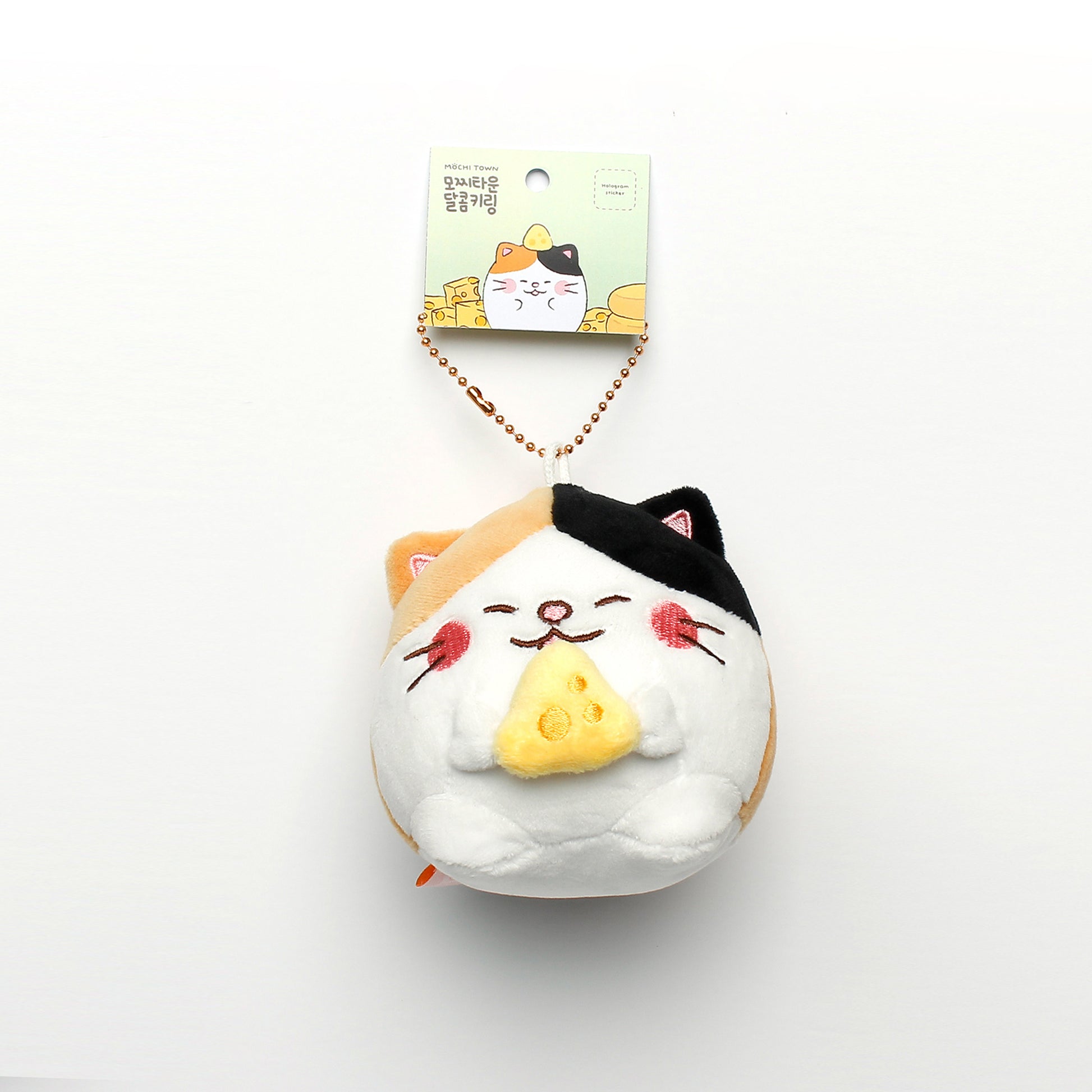Camang (calico cat with cheese) keyring hanging from tag on white background.