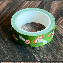Load image into Gallery viewer, The roll of forest green washi tape with red and white amanita mushrooms. Faint painterly skulls are applied over the mushroom caps.
