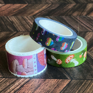 The Pride Hearts washi tape is featured among two other washi tapes in a pile on a wooden table.