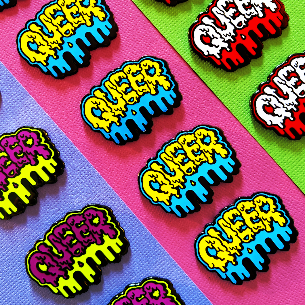 The blue and yellow Queer enamel pin is showcased with other color varieties. Goopy yellow letters spell out 