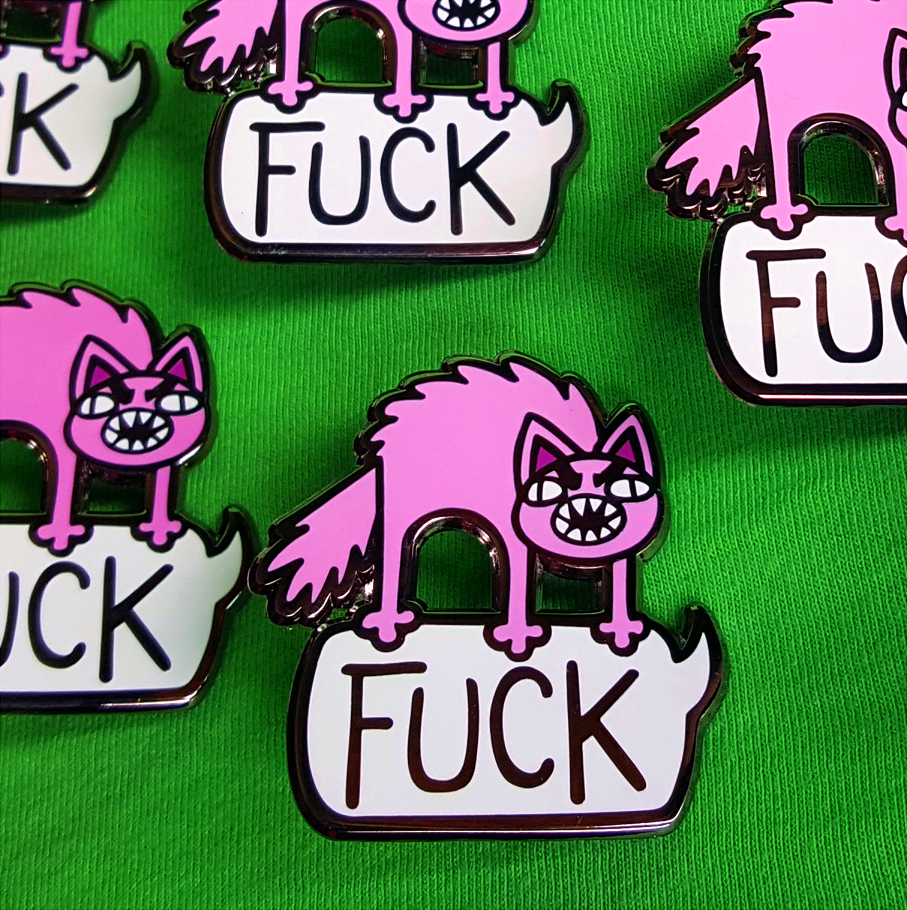 Closeup of many Foul Meowthed Enamel pins. An angry, bristled pink cat stands atop a giant speech bubble, saying 