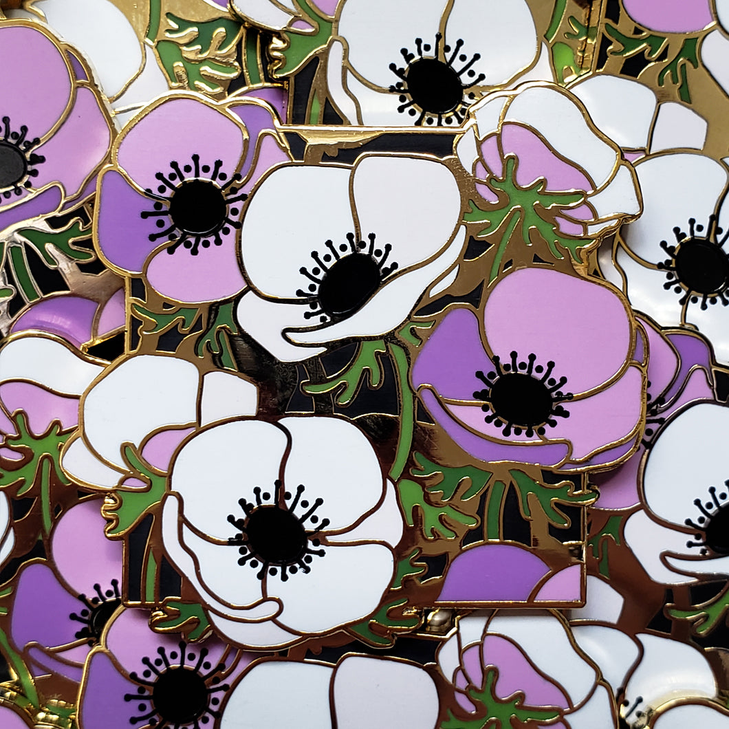 Closeup of the gold cast pin which features a bundle of anemone flowers. The flowers are the colors of the asexual flag (white and purple).