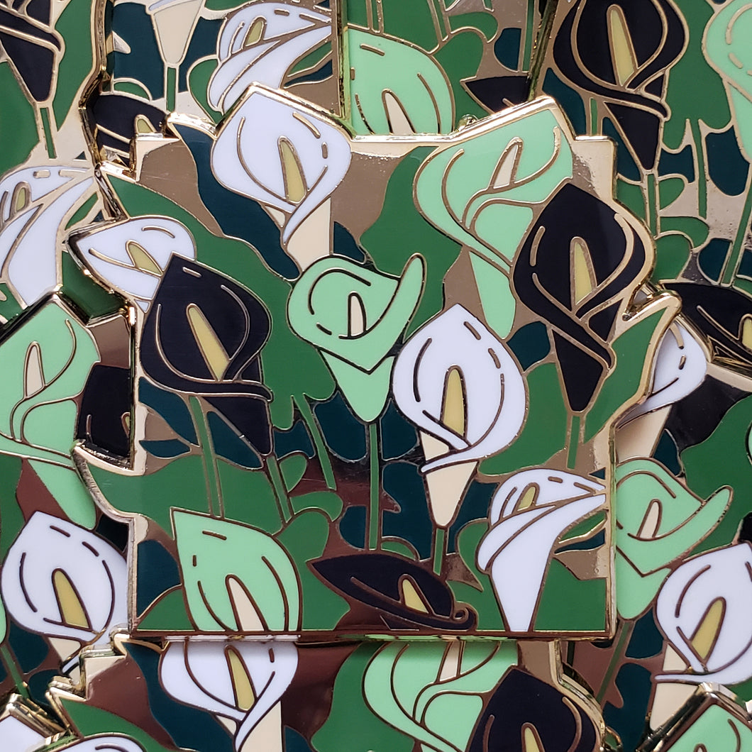 Closeup of the gold cast pin which features a bundle of calla lily flowers. The flowers are the colors of the agender flag (white, green, and black).