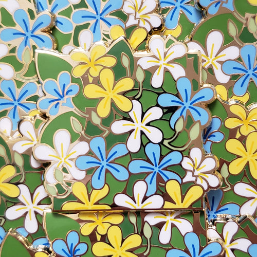 Closeup of the gold cast pin which features a bundle of jasmine flowers. The flowers are the colors of the aroace flag (white, blue, and yellow).