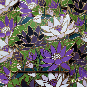 Closeup of the gold cast pin which features a bundle of lotus flowers. The flowers are the colors of the demisexual flag (white, black, and purple).