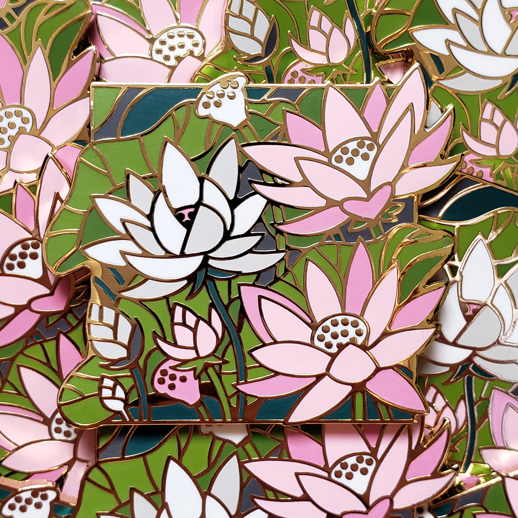 Closeup of the gold cast pin which features a bundle of lotus flowers. The flowers are the colors of the demigirl flag (white and pink).