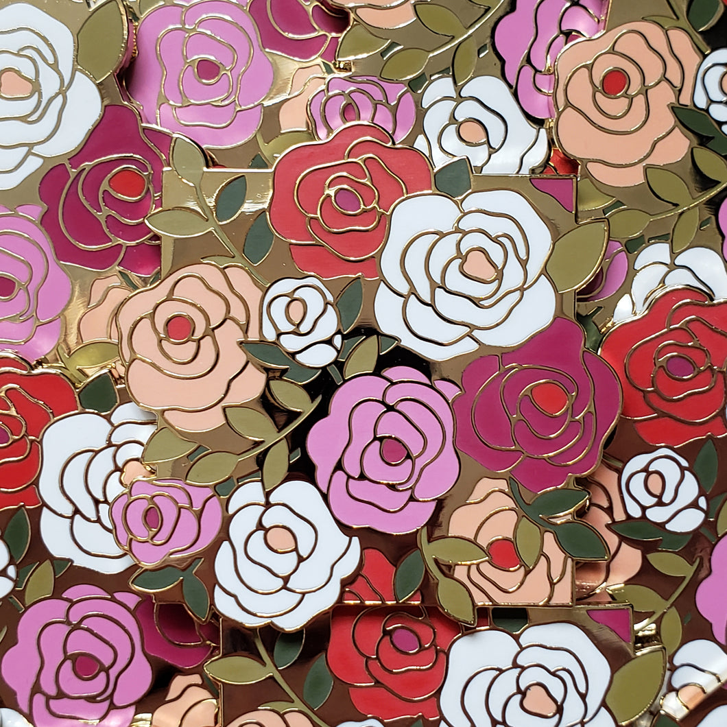 Closeup of the gold cast pin which features a bundle of roses. The flowers are the colors of the lesbian flag (orange, white, pink and purple).