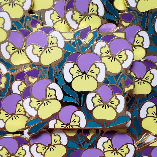 Closeup of the gold cast pin which features a bundle of pansies. The flowers are the colors of the nonbinary flag (yellow, purple, and white).