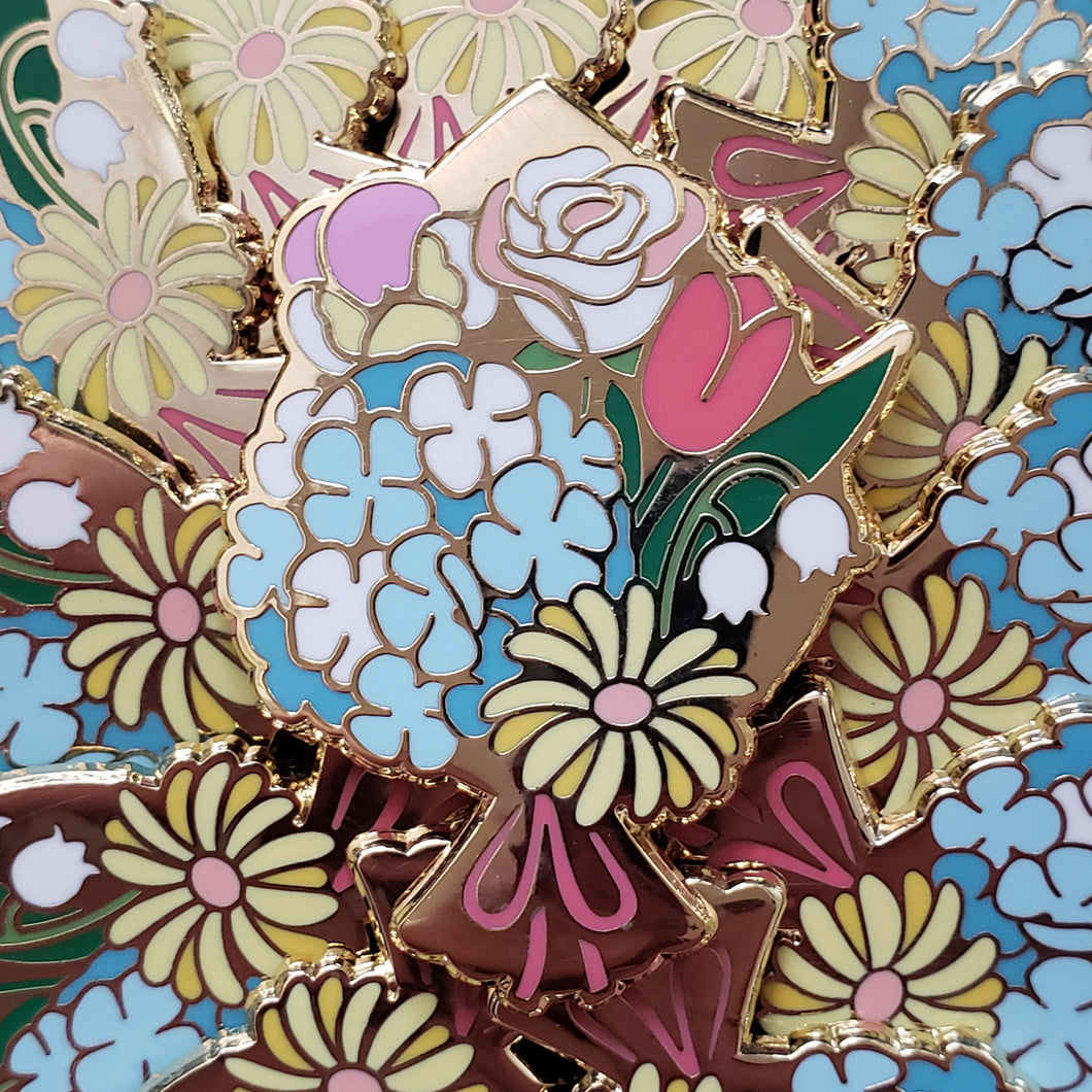 Closeup of the gold cast pin which features a golden bouquet of five kinds of flowers. The flowers are all the colors of pride in a more pastel hue.