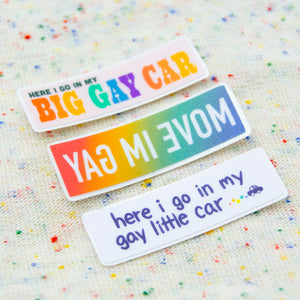 Three mini stickers reading "here i go in my big gay car," "move i'm gay" and "here i go in my gay little car." The Move I'm Gay sticker is printed backwards in order to be seen in a mirror. The here i go in my gay little car sticker features a tiny cartoon car with rainbow exhaust.