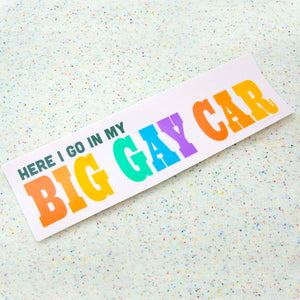 Bumper sticker with a light pin background reads "here i go in my" in small dark green text and "BIG GAY CAR" in large rainbow text.