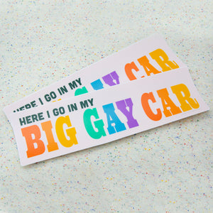 Two "here i go in my big gay car" bumper stickers rest together on a funfetti fabric background.