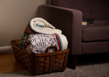 Load image into Gallery viewer, A folded Tortall blanket inside a wicker basket next to a couch. &quot;THE ROOF OF THE WORLD&quot; portion of the illustration is visible on the blanket.