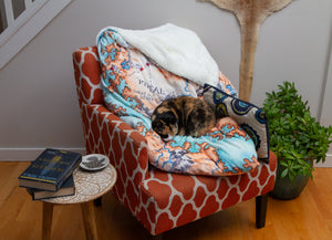 A wider shot of a calico cat taking a nap on the Tortall blanket.