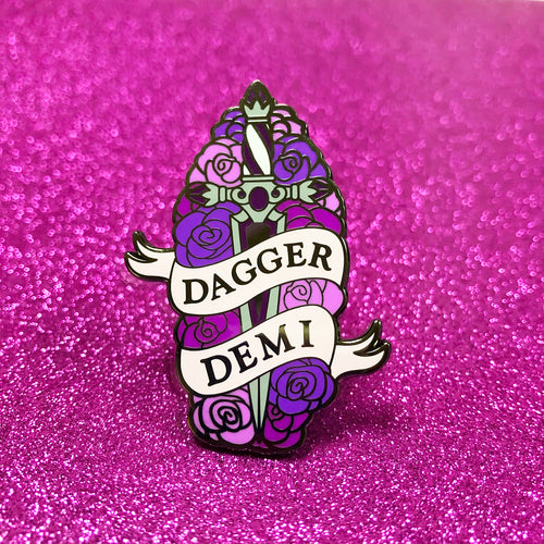The goldcast pin features a decorative dagger in a bed of roses in the purple and pink colors of the demi flag. A ribbon trails across the front and reads 