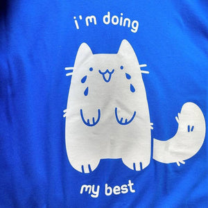 A bright blue t-shirt with white print of a stylized cat smiling and crying. White printed text around the cat reads "I'm doing my best."