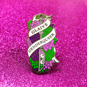 The goldcast pin features a glaive in a bed of roses in the green and purple colors of the genderqueer flag. A ribbon trails across the front and reads "Glaive Genderqueer"