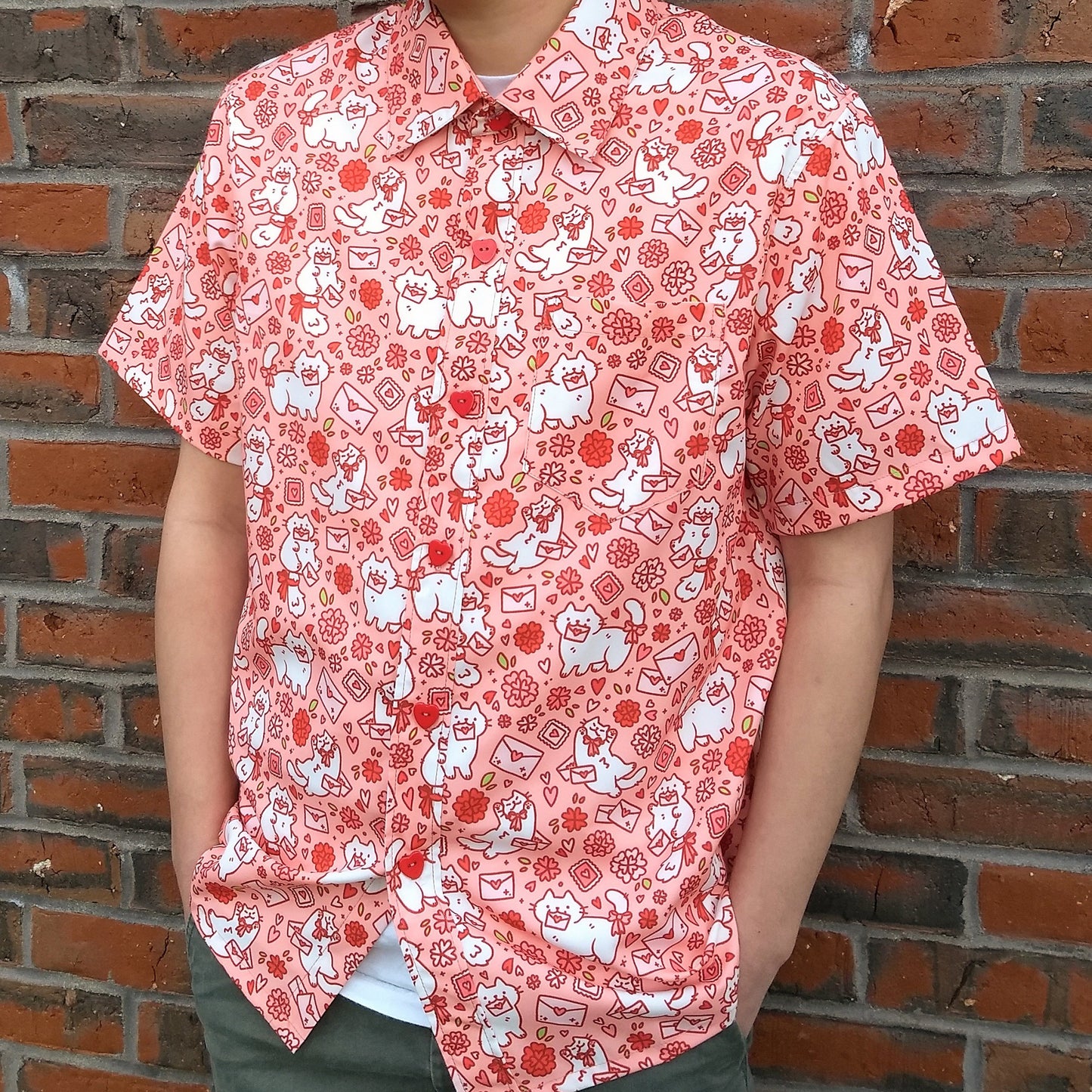 A model stands relaxed wearing the Love Letter Button-up, the bright shirt colors popping against a brick wall in the background.