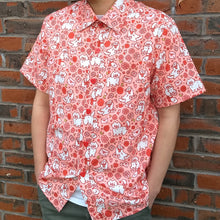 Load image into Gallery viewer, A model stands relaxed wearing the Love Letter Button-up, the bright shirt colors popping against a brick wall in the background.