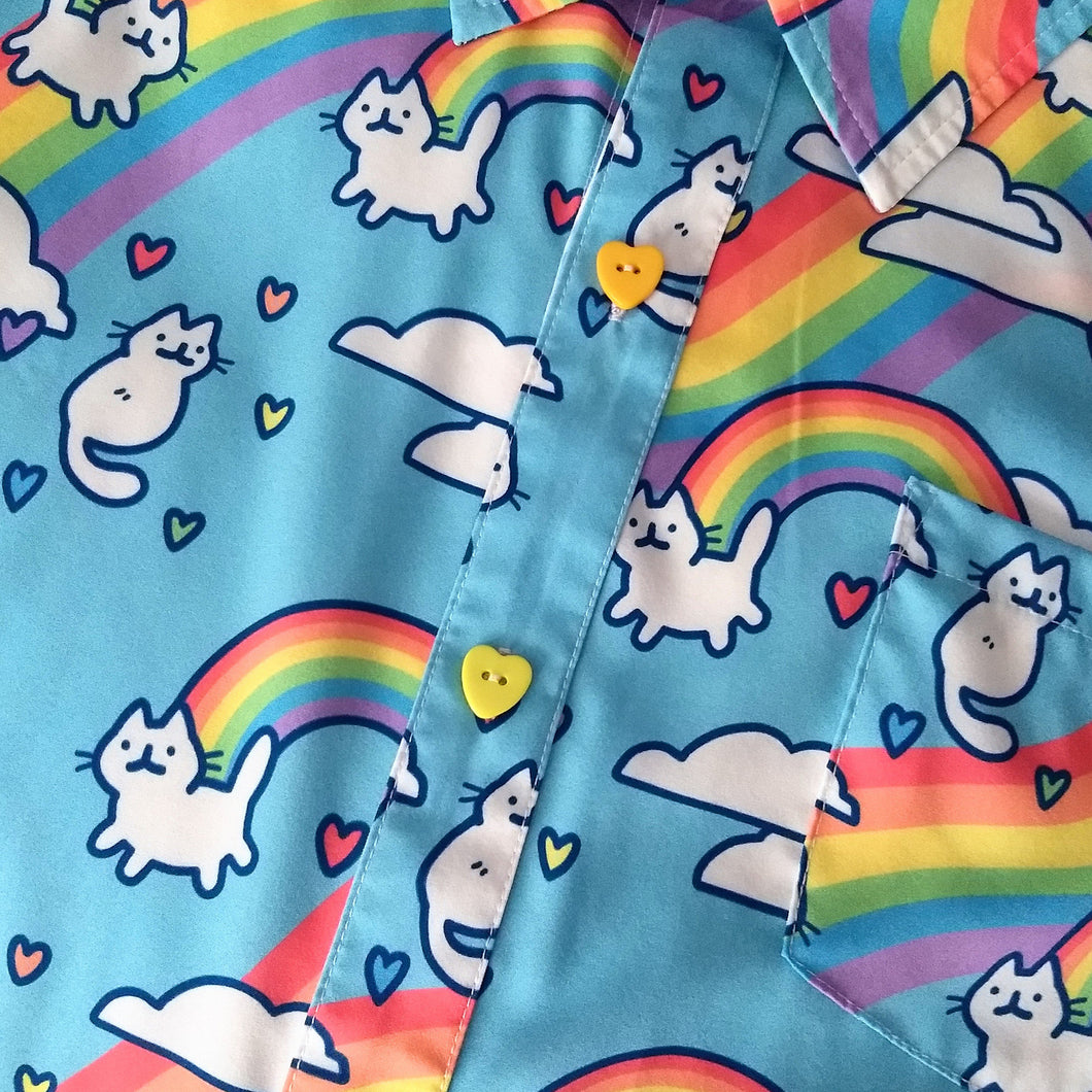 A sky blue button up shirt with heart shaped yellow buttons. The shirt pattern features cute white cats, white clouds, and rainbows. Sometimes the white cats serve in place of clouds at the ends of the rainbows.