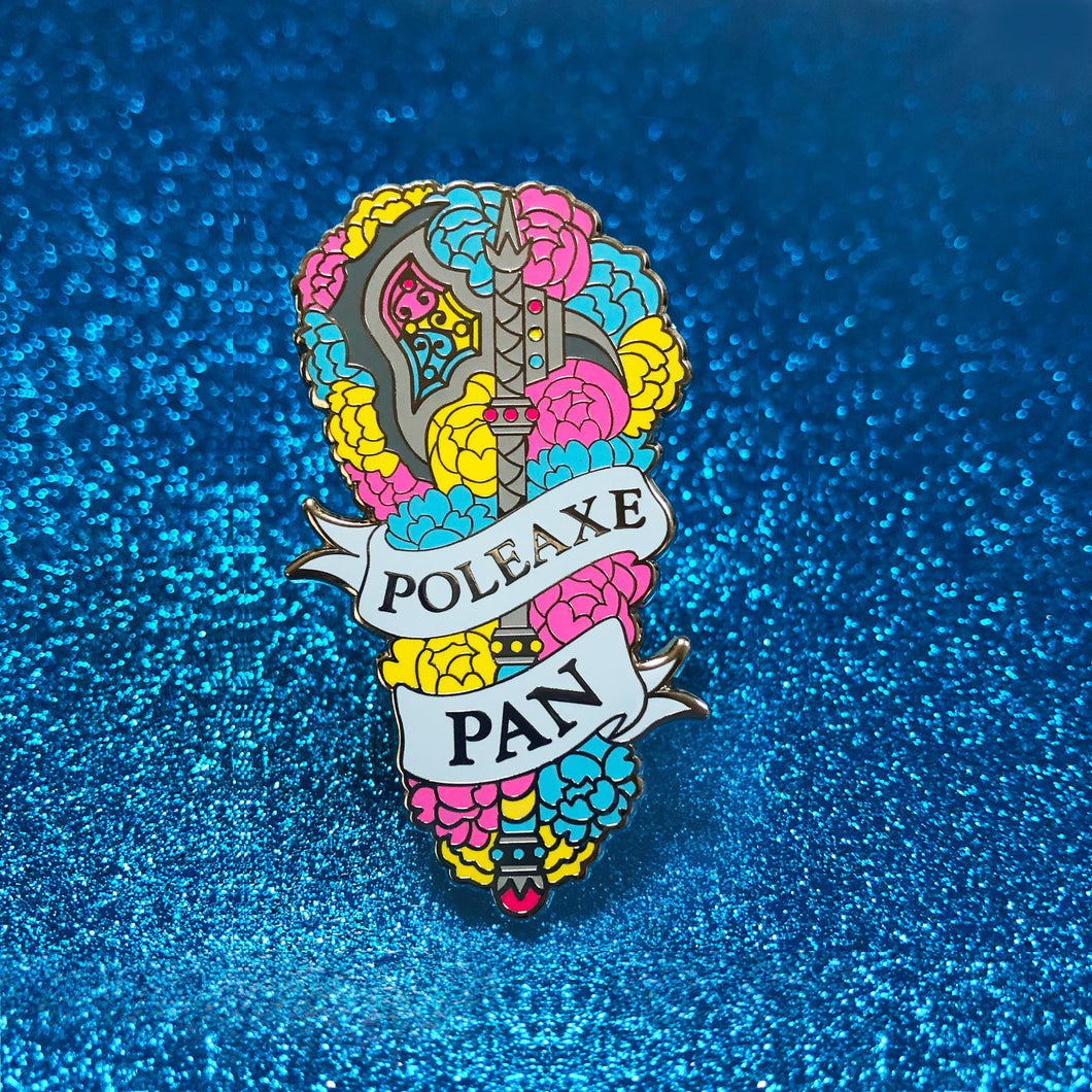 The goldcast pin features a decorative poleaxe in a bed of roses in the blue, yellow, and pink colors of the pansexual flag. A ribbon trails across the front and reads 