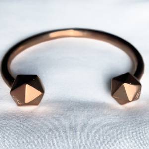 Rose gold D20 Dice bangle on white fabric.