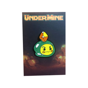 Green, yellow, and orange Undermine Pilfer character Enamel pin on Undermine dark cave art backing card.