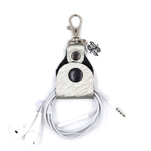 Load image into Gallery viewer, Silver leather headphone keepers with Dual Wield Studio logo and silver clasp holding white aux headphones on white background.