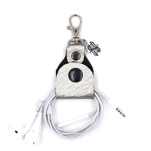Silver leather headphone keepers with Dual Wield Studio logo and silver clasp holding white aux headphones on white background.