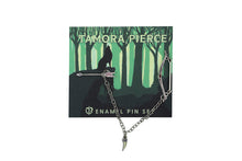 Load image into Gallery viewer, Set of silver bow and arrow enamel pins connected by a delicate chain with a badger claw charm hanging from it. Pins are on a green Tamora Pierce backing card depicting a howling wolf in the woods.