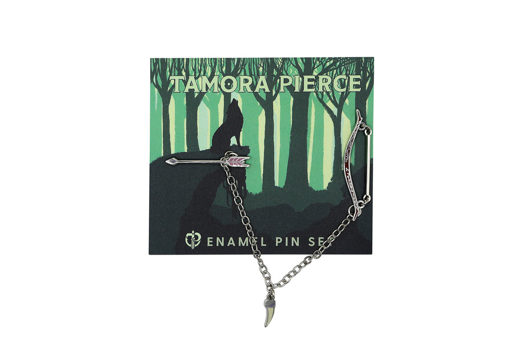 Set of silver bow and arrow enamel pins connected by a delicate chain with a badger claw charm hanging from it. Pins are on a green Tamora Pierce backing card depicting a howling wolf in the woods.
