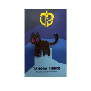 Black cat enamel pin with purple eyes, frowning on Blue Tamora Pierce backing card with white background.