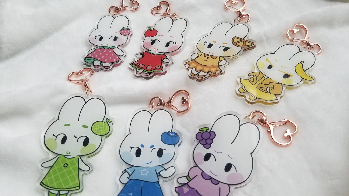 Closeup of all fruit bunny acrylic charms on white blanket.