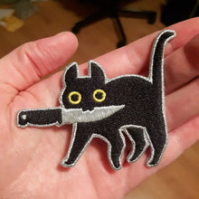 Load image into Gallery viewer, Embroidered patch depicting a black cat with yellow eyes holding knife in mouth in model&#39;s hand.