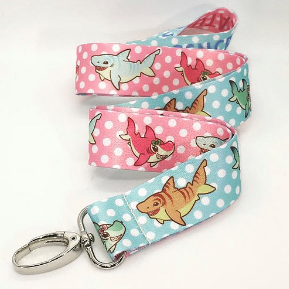 Light pink and light blue polka dot lanyard with cute shark illustrations on white packground.