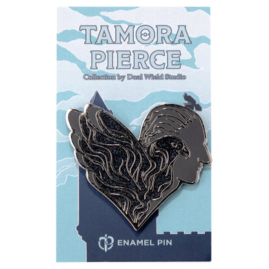 Glittering black and grey enamel pin that shows a hawk in profile, and Numair in profile behind it. The whole pin evokes a heart shape and is pinned to a light blue castle Tamora Pierce backing card.