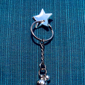 Silver star charm pin holding silver keyring with charms on turquoise cloth background.