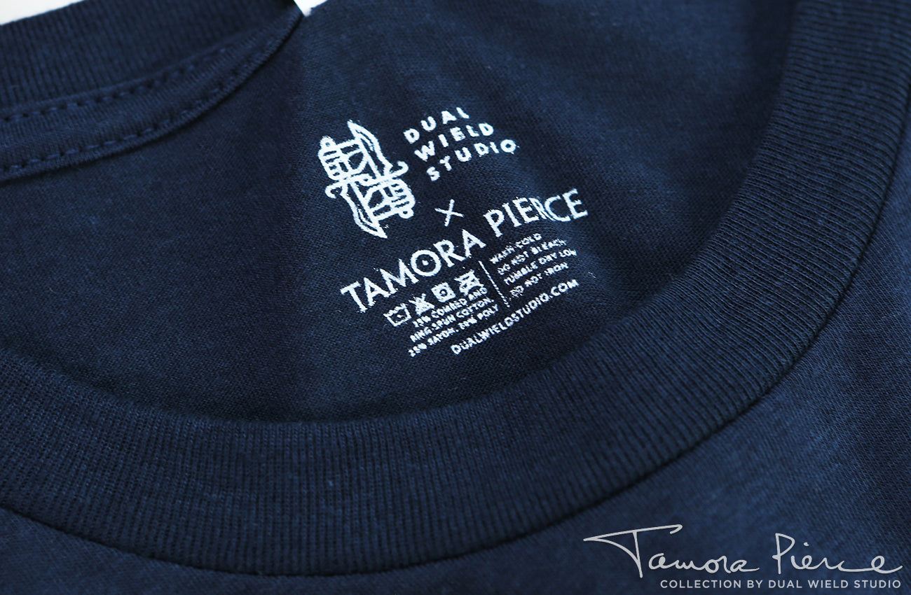 Closeup of printed-on Dual Wield Studio x Tamora Pierce tag with garment care below.