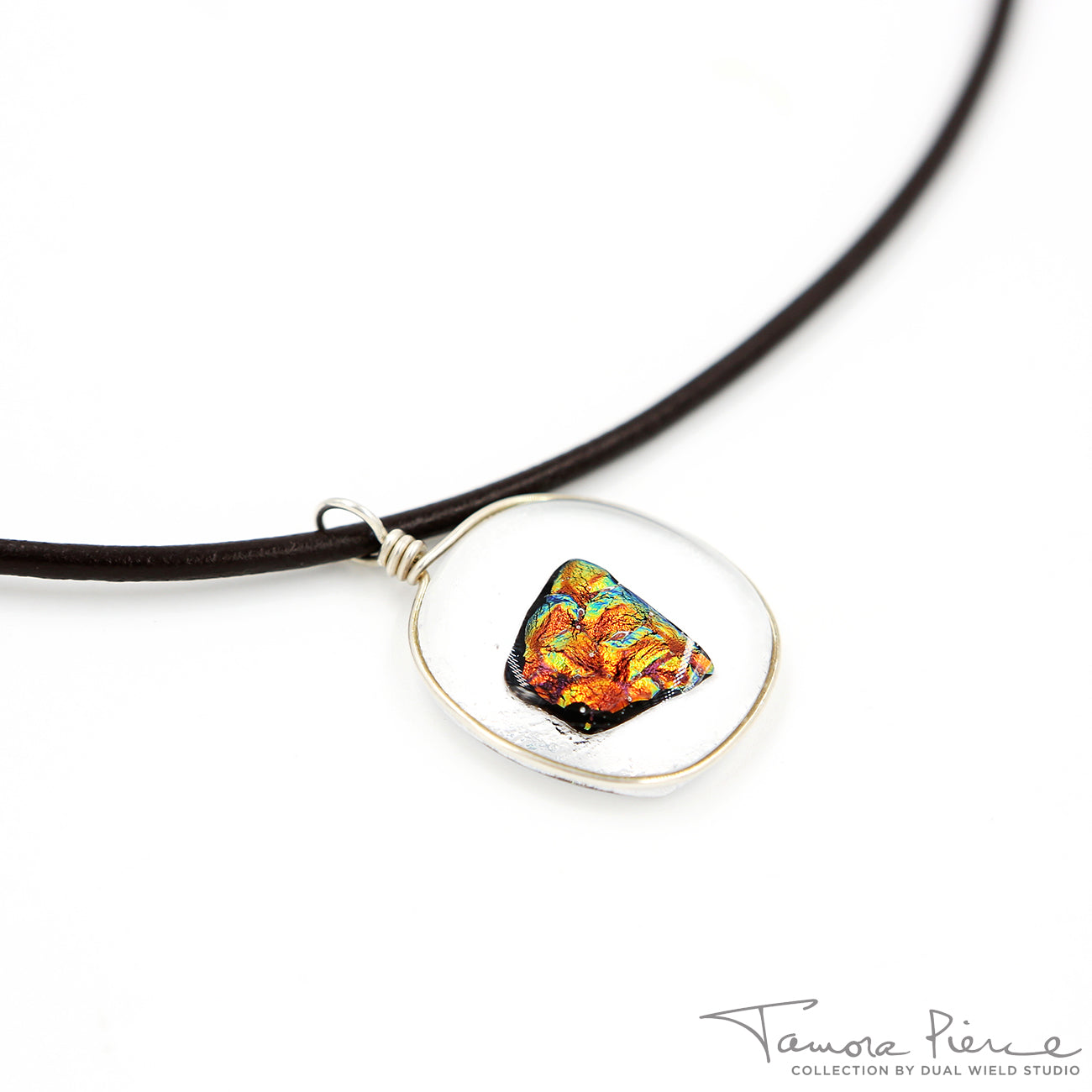A molten lava-like looking stone with azure details floating in a gold-rimmed, circular glass pendant. Pendant is on brown necklace cord with white background.