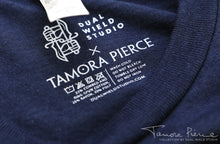 Load image into Gallery viewer, Closeup of printed-on Dual Wield Studio x Tamora Pierce tag with garment care below.